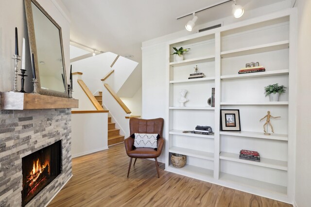 sitting room with stairs, a warm lit fireplace, visible vents, and wood finished floors