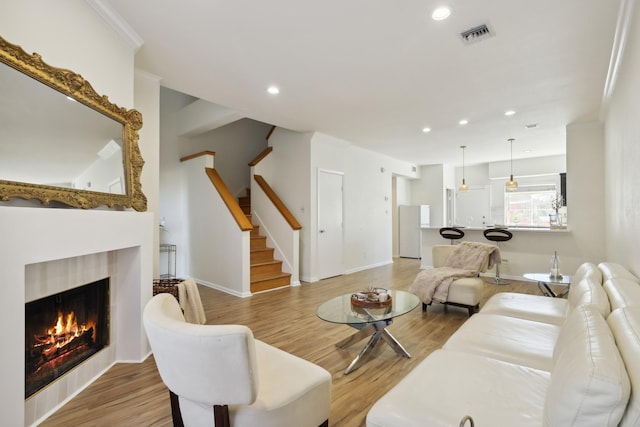 living area featuring visible vents, light wood-style flooring, a lit fireplace, stairs, and recessed lighting