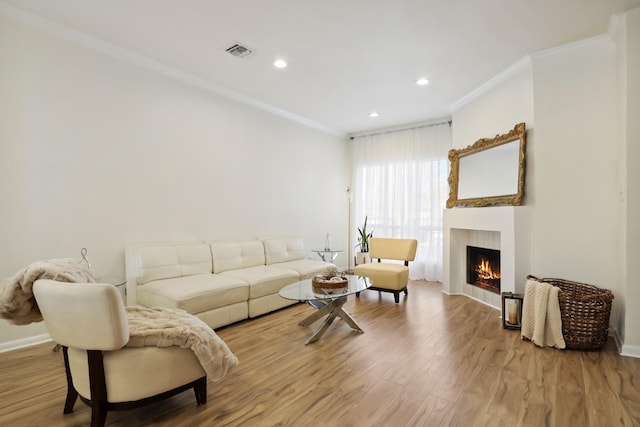 living room with a warm lit fireplace, visible vents, crown molding, and light wood finished floors