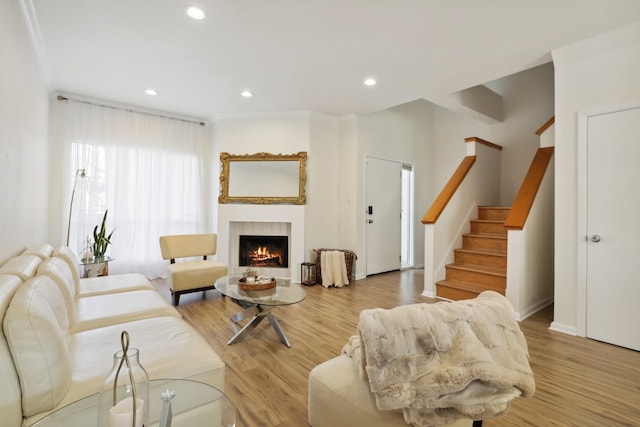 living room featuring recessed lighting, a lit fireplace, stairway, and wood finished floors