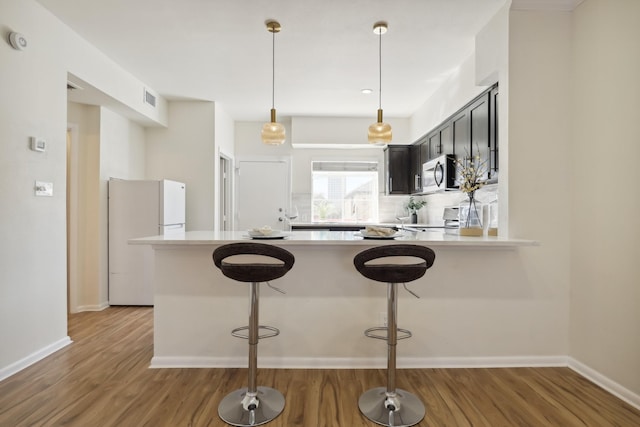 kitchen featuring light countertops, stainless steel microwave, freestanding refrigerator, wood finished floors, and a peninsula