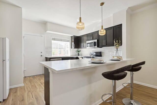 kitchen with light wood-style flooring, a breakfast bar area, a peninsula, stainless steel appliances, and light countertops