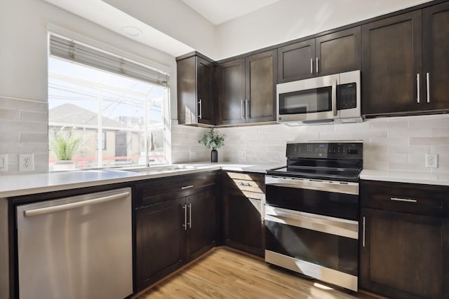 kitchen with light wood finished floors, decorative backsplash, appliances with stainless steel finishes, light countertops, and dark brown cabinets