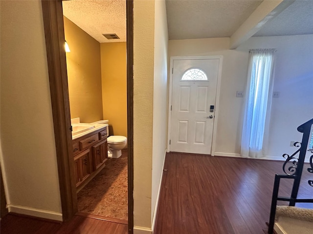 foyer entrance featuring dark wood-style flooring, visible vents, a textured ceiling, and baseboards