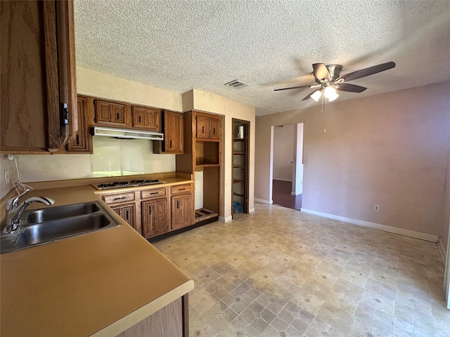 kitchen featuring brown cabinets, light floors, gas stovetop, a sink, and under cabinet range hood