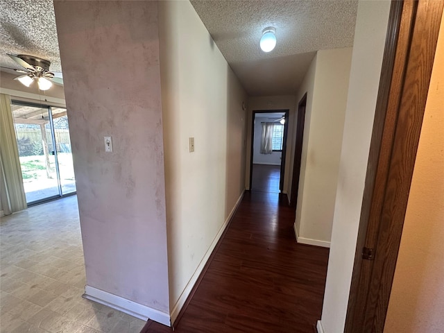 corridor featuring baseboards, a textured ceiling, and wood finished floors