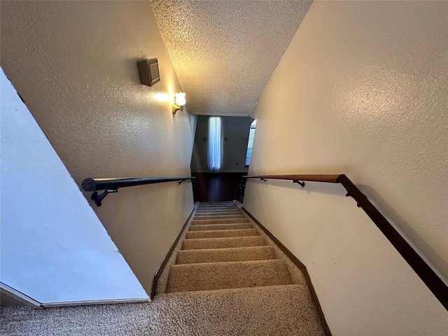 staircase featuring a textured ceiling, carpet floors, a textured wall, and baseboards