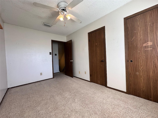 unfurnished bedroom featuring a textured ceiling, baseboards, visible vents, and light colored carpet