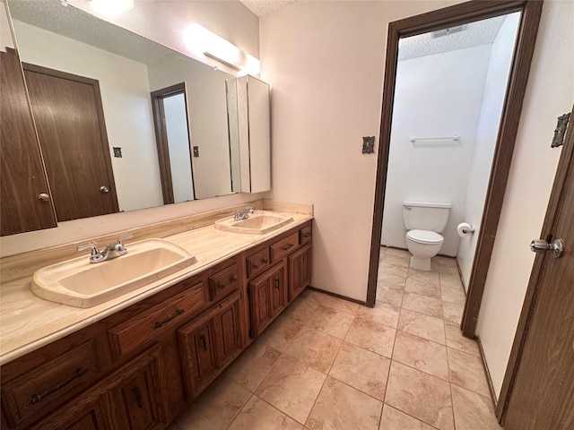 bathroom with toilet, a textured ceiling, double vanity, and a sink