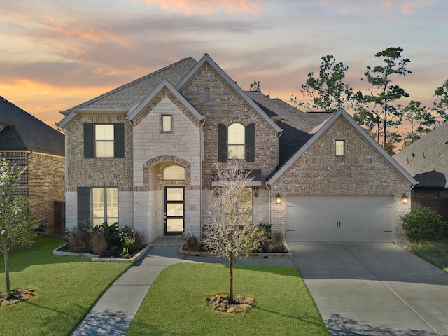 french country home featuring a garage, a shingled roof, a lawn, and brick siding