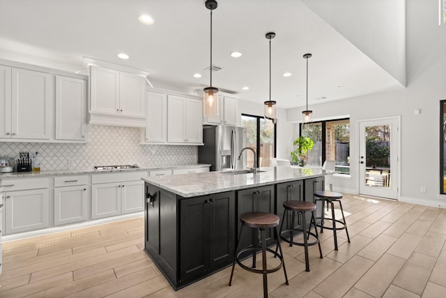 kitchen with a sink, white cabinetry, stainless steel refrigerator with ice dispenser, decorative backsplash, and a center island with sink