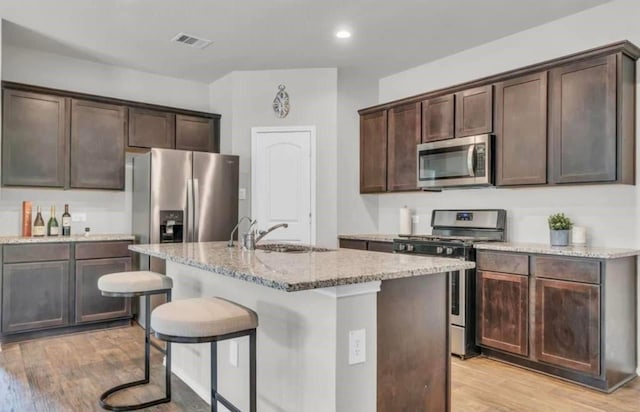 kitchen featuring visible vents, light wood finished floors, a sink, stainless steel appliances, and dark brown cabinets