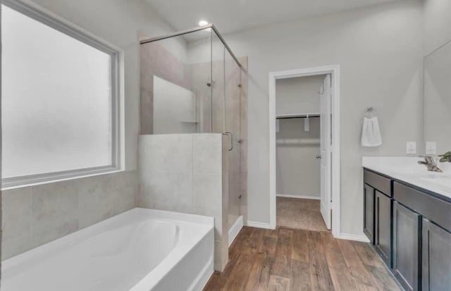 bathroom featuring wood finished floors, a shower stall, a spacious closet, a bath, and vanity