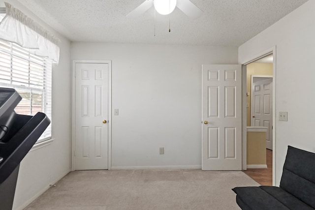 living area featuring a ceiling fan, light colored carpet, a textured ceiling, and baseboards