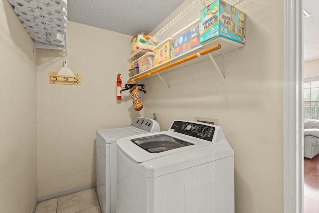 washroom with laundry area, light tile patterned floors, baseboards, washer and clothes dryer, and a textured ceiling