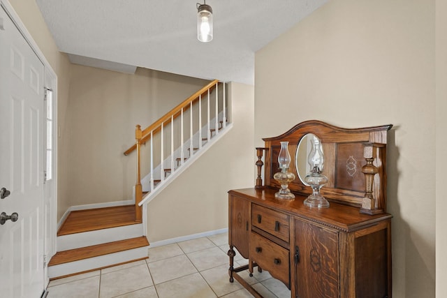 tiled foyer entrance with stairs, baseboards, and a textured ceiling