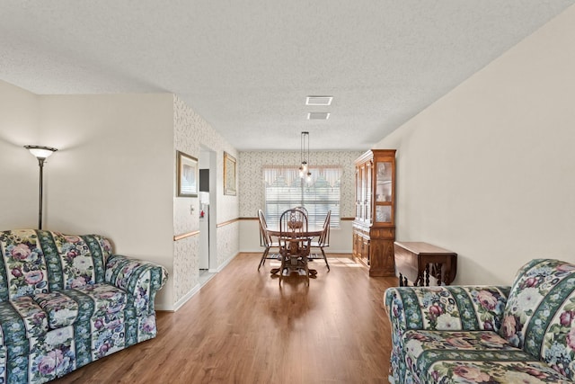 dining space with a textured ceiling, baseboards, wood finished floors, and wallpapered walls