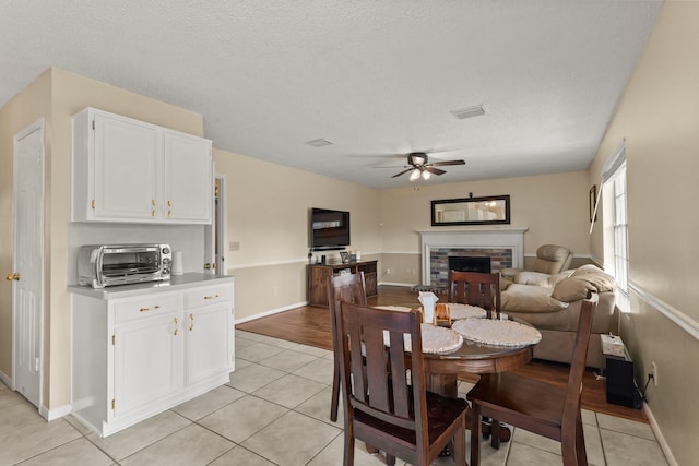 dining area with a toaster, ceiling fan, a stone fireplace, and light tile patterned flooring