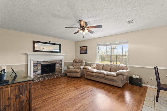 living room with ceiling fan, a textured ceiling, a fireplace, visible vents, and light wood-type flooring