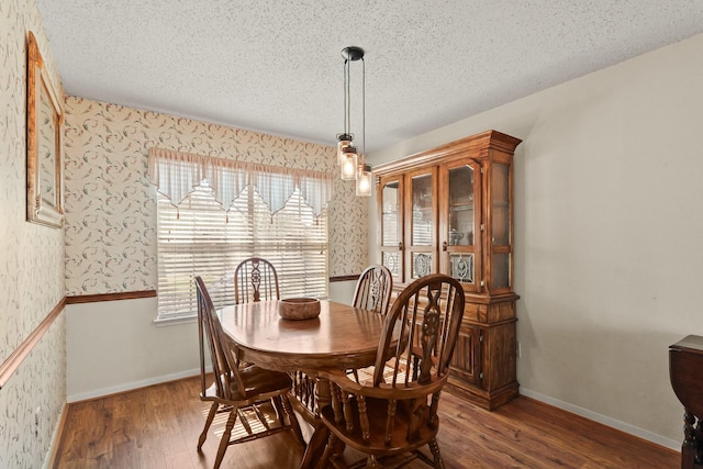 dining room featuring wood finished floors, wainscoting, a textured ceiling, and wallpapered walls