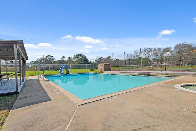 view of pool featuring a lawn, fence, a water slide, an outdoor structure, and a shed