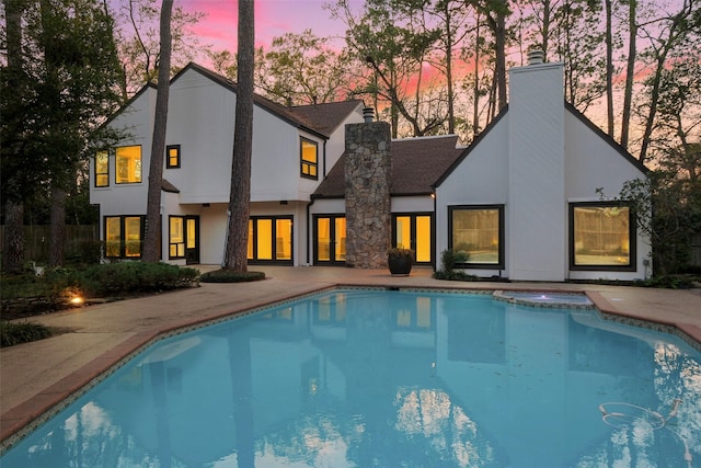 back of property with stucco siding, a chimney, and a pool with connected hot tub