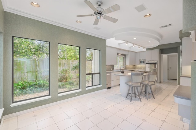 kitchen with visible vents, a breakfast bar, ornamental molding, a ceiling fan, and appliances with stainless steel finishes