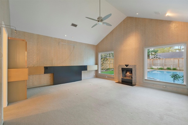 unfurnished living room with visible vents, carpet, a fireplace with flush hearth, high vaulted ceiling, and a ceiling fan