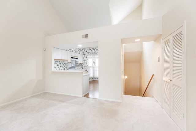 unfurnished room with baseboards, high vaulted ceiling, visible vents, and light colored carpet