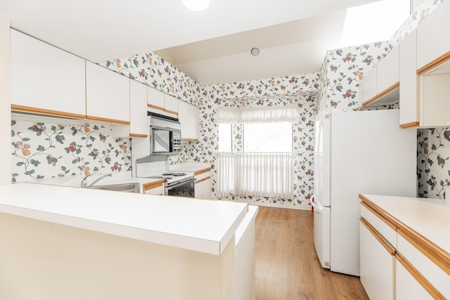 kitchen featuring a peninsula, white appliances, a sink, light wood-style floors, and light countertops