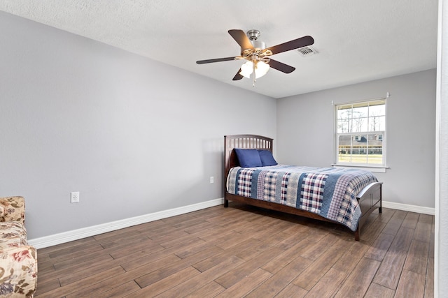 bedroom with a ceiling fan, visible vents, baseboards, and wood finished floors