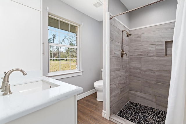 full bathroom with visible vents, a tile shower, toilet, and wood finished floors