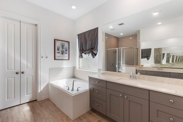 bathroom featuring visible vents, a stall shower, wood finished floors, a bath, and vanity