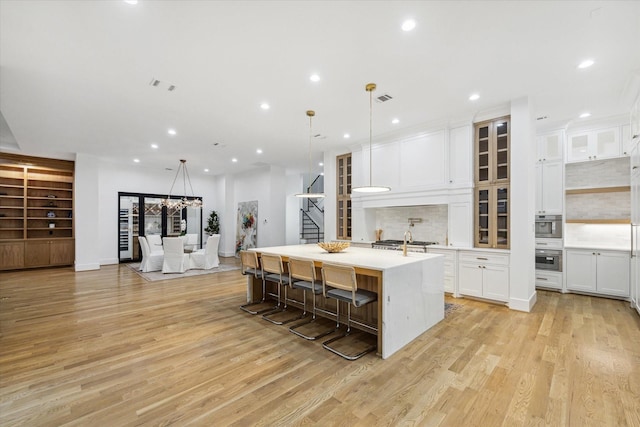 kitchen featuring visible vents, white cabinets, a large island with sink, and oven