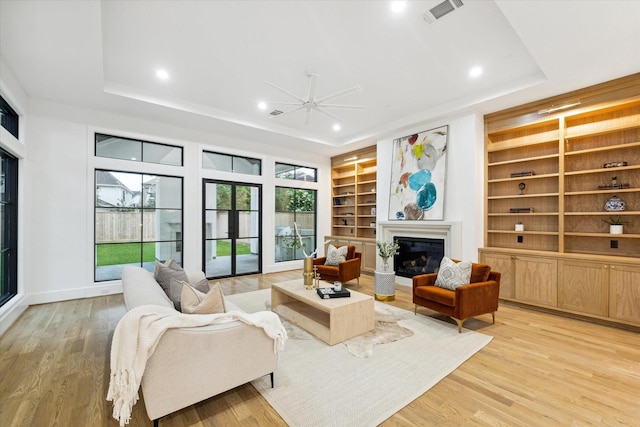 interior space with a glass covered fireplace, a raised ceiling, visible vents, and light wood-style floors