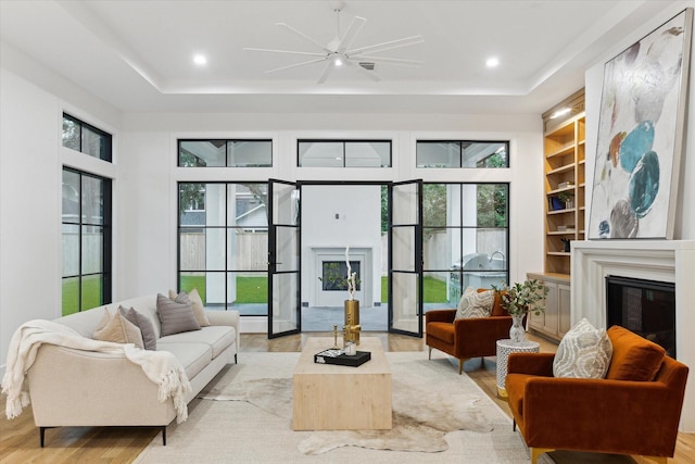 interior space featuring built in shelves, a glass covered fireplace, light wood-type flooring, and a raised ceiling