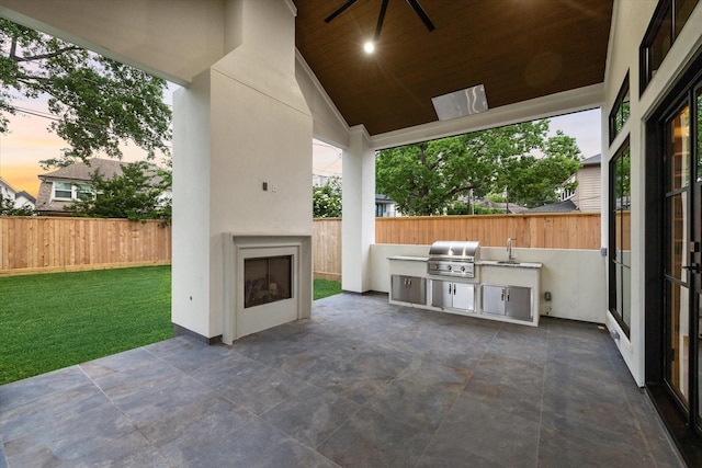 view of patio / terrace with grilling area, a sink, exterior kitchen, a fenced backyard, and an outdoor fireplace