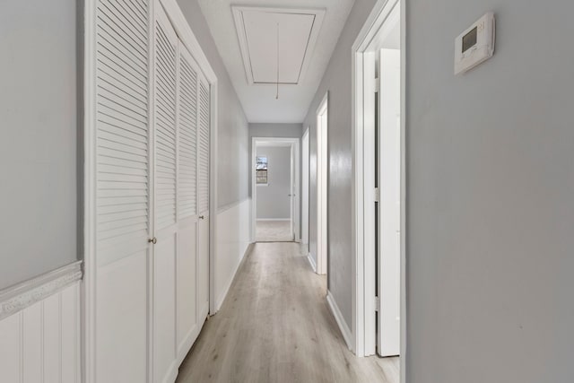 corridor featuring a wainscoted wall, attic access, and light wood-style flooring