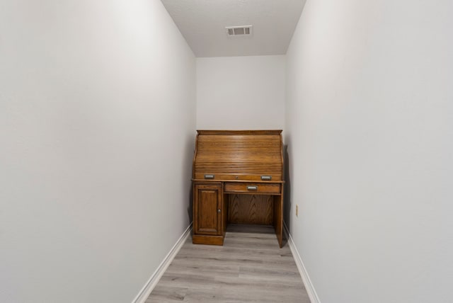 corridor featuring light wood-style flooring, a textured ceiling, visible vents, and baseboards