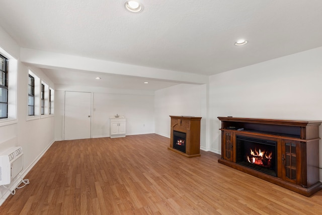 unfurnished living room with recessed lighting, baseboards, a lit fireplace, a wall mounted AC, and light wood finished floors