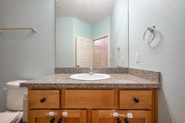 bathroom with a textured wall, vanity, and toilet