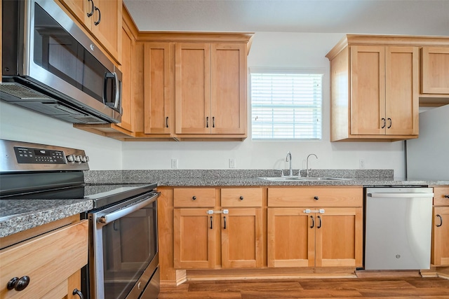 kitchen featuring appliances with stainless steel finishes, dark countertops, a sink, and light wood-style flooring