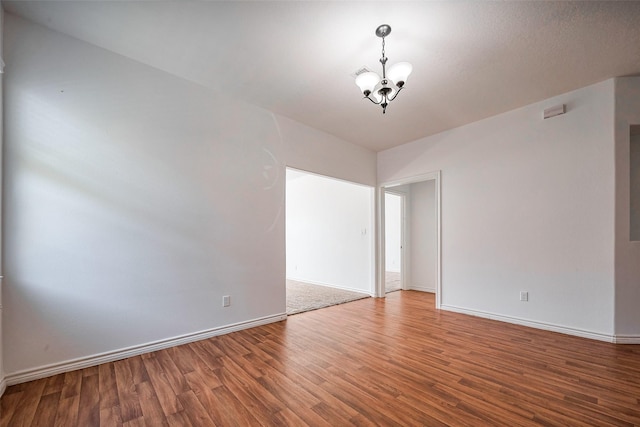 empty room with baseboards, wood finished floors, and an inviting chandelier