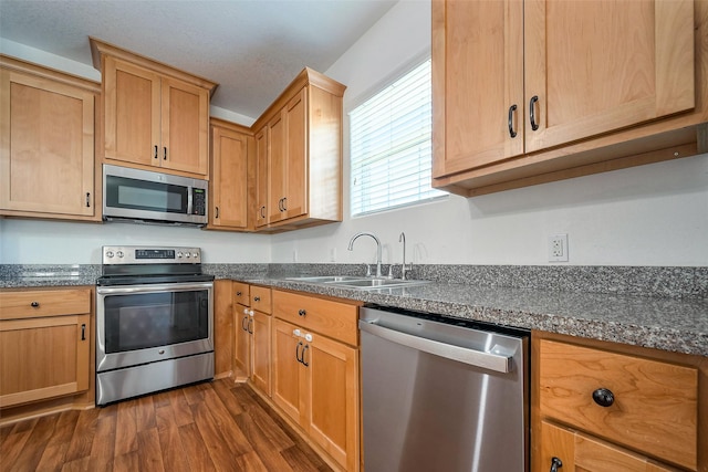 kitchen with stainless steel appliances, dark countertops, dark wood-type flooring, and a sink