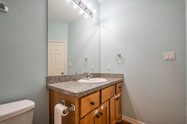 bathroom with a textured wall, vanity, and toilet