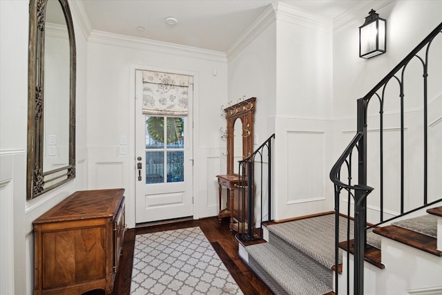 foyer entrance with dark wood-style floors, a decorative wall, stairway, ornamental molding, and wainscoting