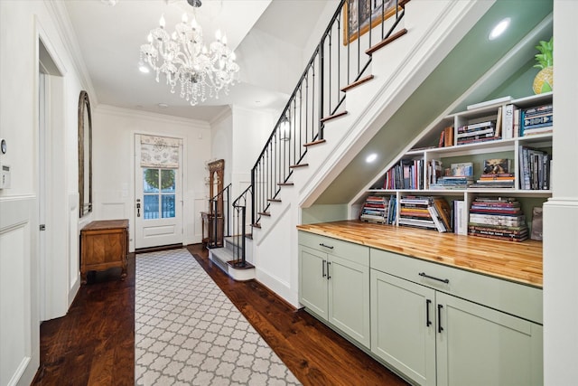 foyer entrance featuring stairs, ornamental molding, dark wood finished floors, and a notable chandelier