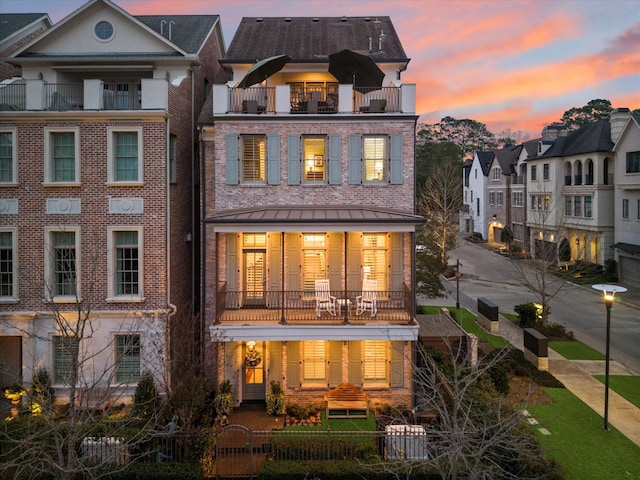 rear view of property featuring brick siding, a fenced front yard, and a balcony