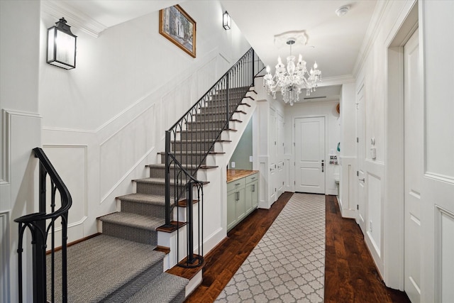 stairs featuring ornamental molding, an inviting chandelier, wood finished floors, and a decorative wall