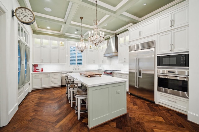 kitchen featuring white cabinets, a kitchen island, glass insert cabinets, built in appliances, and wall chimney range hood